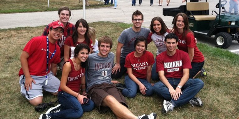 A group of students sitting on a grassy lawn in Indiana University gear, smiling for a photo